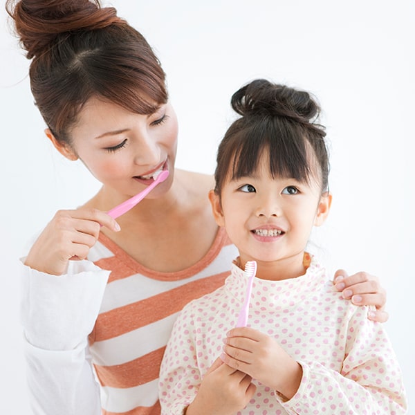 A mother teaching her little daughter to brush her teeth